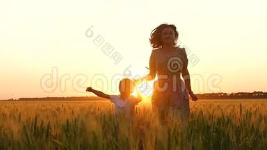一位快乐的母亲牵着孩子的手，在日落时穿过一片麦田。 一个母亲和一个小男孩穿过